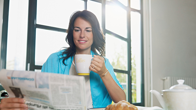 Mujer bebiendo en una taza mientras lee el periódico